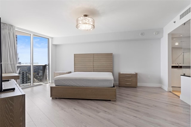 bedroom featuring floor to ceiling windows, light wood-type flooring, access to outside, baseboards, and a sink