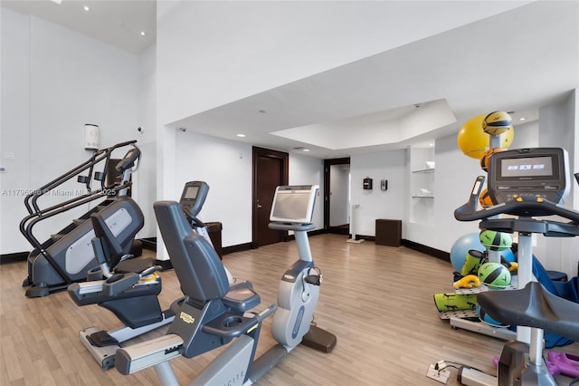 exercise room featuring light wood-style floors, baseboards, and a raised ceiling