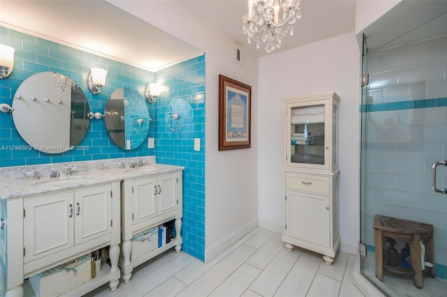 bathroom featuring a shower stall, tile walls, a chandelier, double vanity, and baseboards