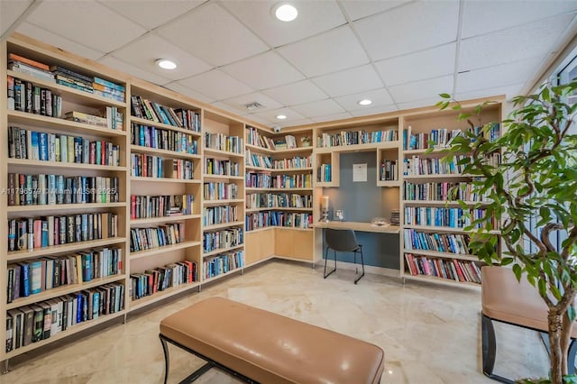 living area featuring wall of books, a paneled ceiling, and built in features