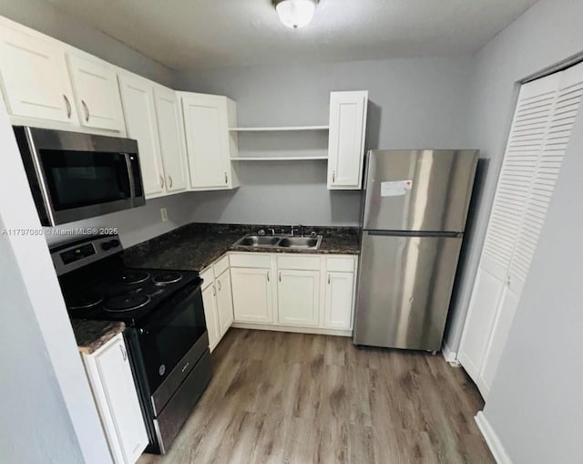 kitchen with a sink, white cabinetry, open shelves, wood finished floors, and appliances with stainless steel finishes