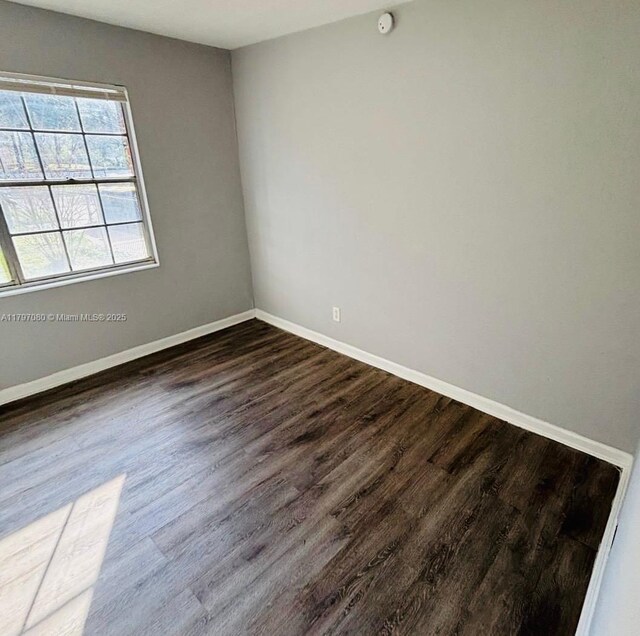 unfurnished room featuring baseboards and dark wood-style floors