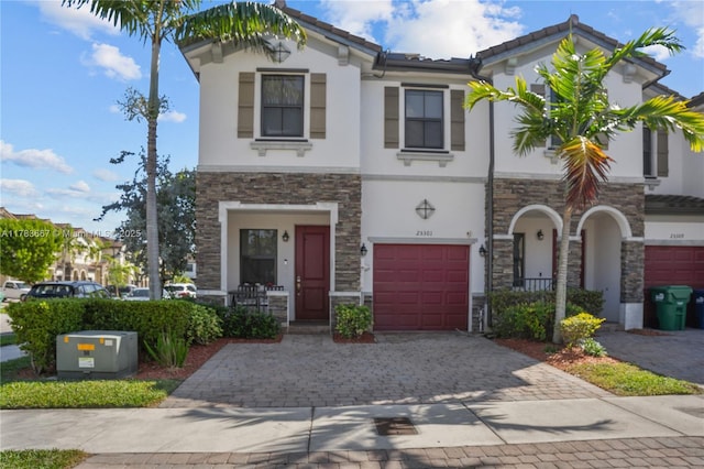 view of front of home featuring stone siding, decorative driveway, stucco siding, and a garage