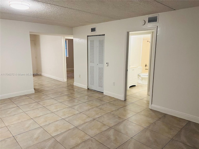 empty room featuring light tile patterned flooring, a textured ceiling, and baseboards