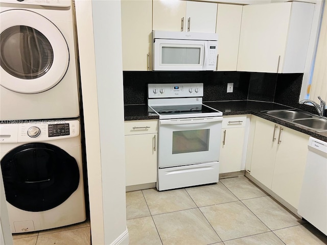 kitchen with white appliances, stacked washer and clothes dryer, a sink, dark countertops, and white cabinetry