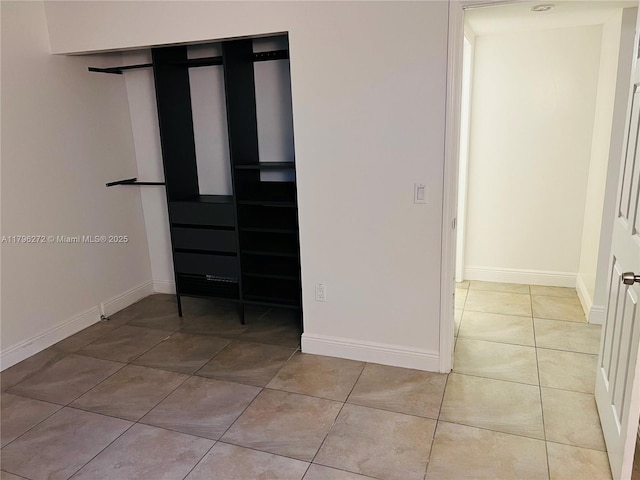 unfurnished bedroom featuring light tile patterned floors, baseboards, and a closet