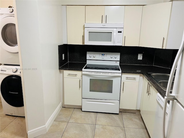 kitchen featuring white appliances, estacked washer and dryer, light tile patterned flooring, and dark countertops