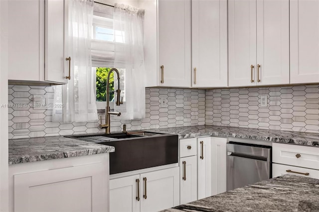 kitchen with a sink, stone counters, white cabinetry, and tasteful backsplash