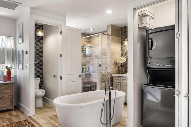 bathroom with vanity, visible vents, stacked washer and clothes dryer, a shower stall, and a soaking tub