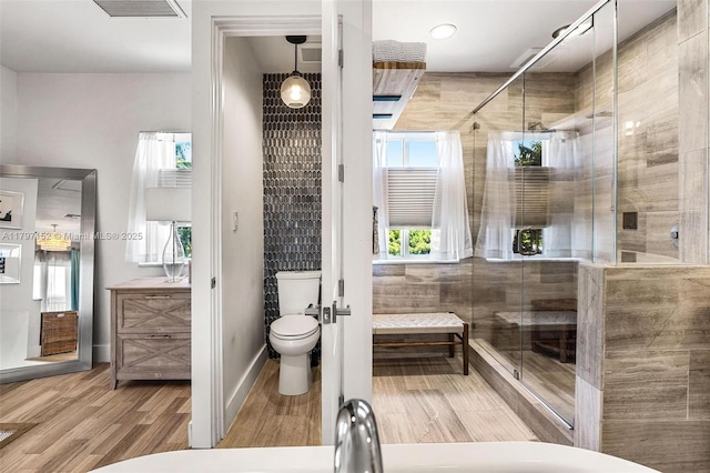 full bath featuring toilet, a wealth of natural light, a shower stall, and wood finished floors