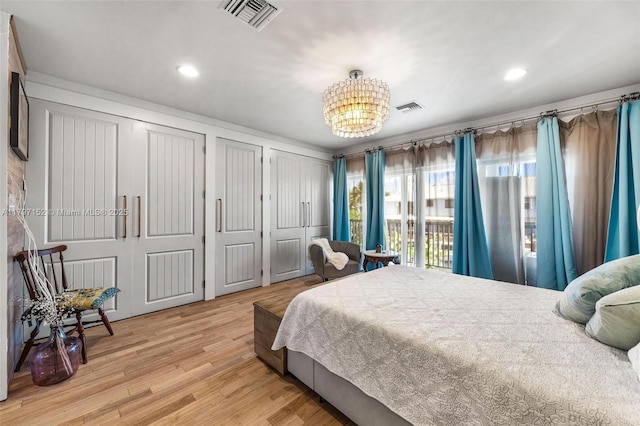 bedroom with multiple closets, wood finished floors, visible vents, and an inviting chandelier
