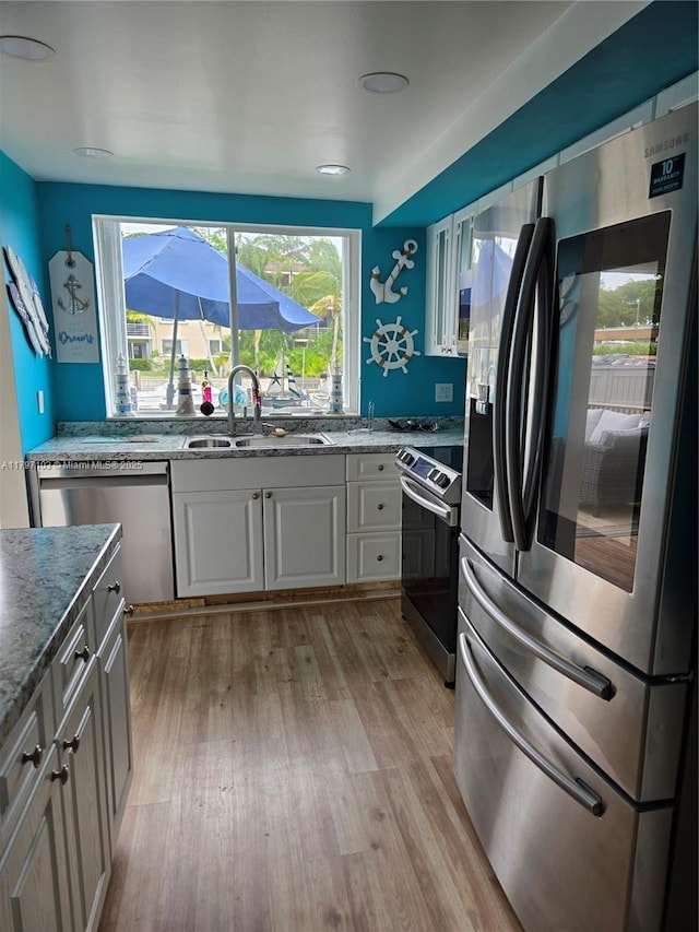 kitchen featuring stone counters, a sink, light wood-style floors, white cabinets, and appliances with stainless steel finishes
