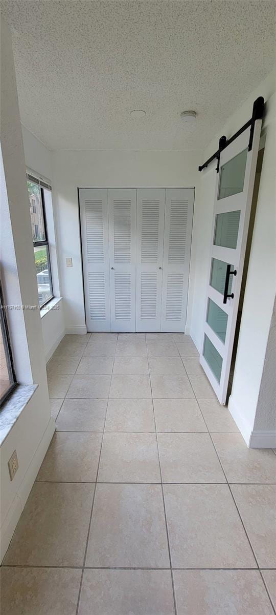 interior space with a textured ceiling, light tile patterned flooring, a barn door, and baseboards