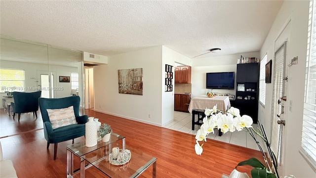 living room with a textured ceiling, a wealth of natural light, baseboards, and light wood-style floors