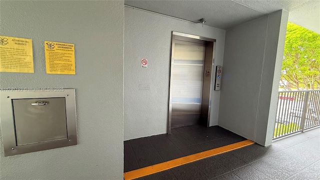 interior space featuring a textured ceiling, a textured wall, and elevator