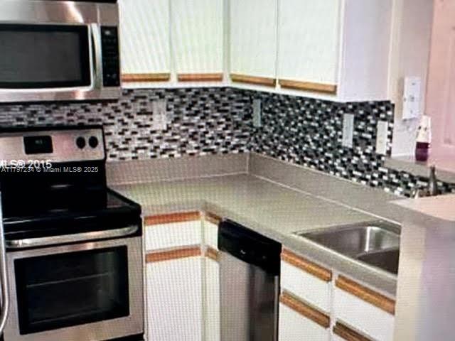 kitchen featuring a sink, stainless steel appliances, backsplash, and white cabinets