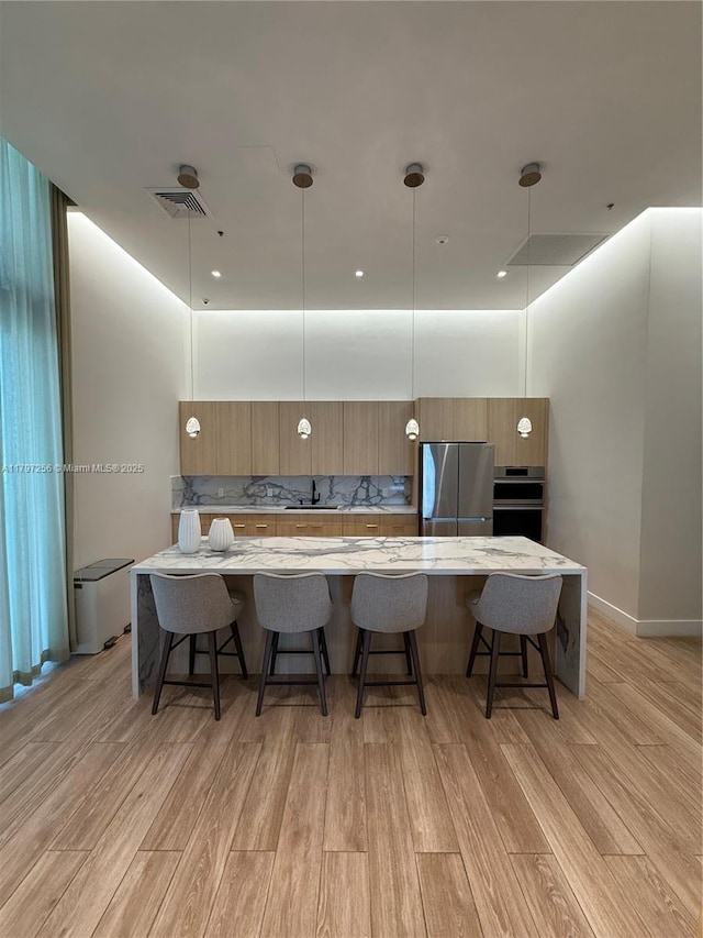 kitchen featuring stainless steel appliances, light wood-style floors, a kitchen bar, and brown cabinetry