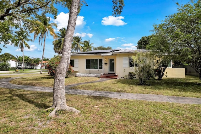 view of front of house featuring a front lawn, roof mounted solar panels, and stucco siding
