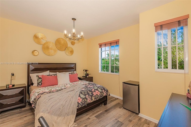 bedroom featuring baseboards, a notable chandelier, stainless steel fridge, and wood finished floors