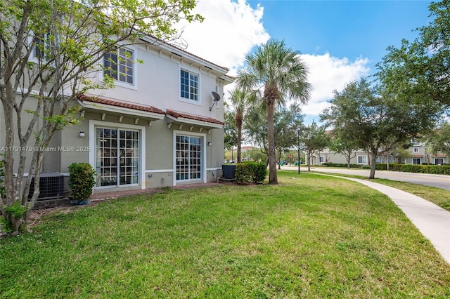 back of house featuring cooling unit, stucco siding, a tile roof, and a lawn