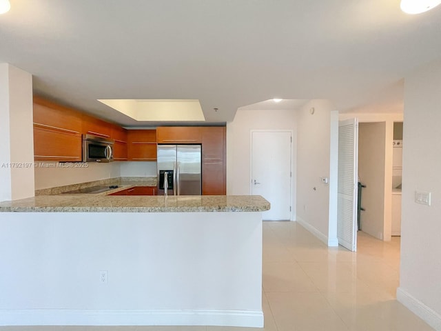 kitchen featuring stainless steel appliances, brown cabinetry, baseboards, a peninsula, and light countertops