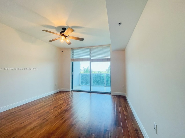 empty room featuring dark wood finished floors, baseboards, a ceiling fan, and a wall of windows