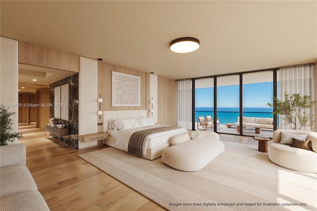 bedroom featuring floor to ceiling windows, light wood-style floors, a water view, and access to exterior