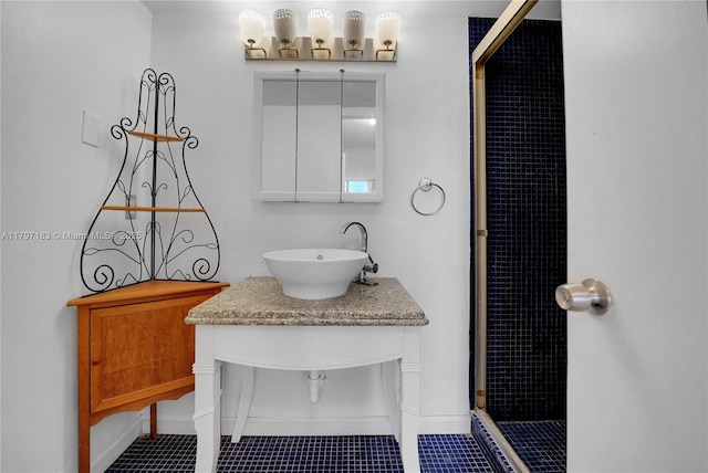 bathroom featuring a sink, baseboards, tiled shower, and tile patterned floors