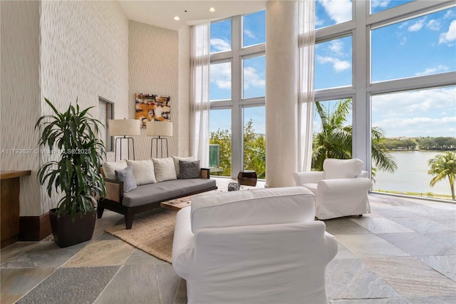 living area featuring a towering ceiling, a water view, stone finish floor, and recessed lighting