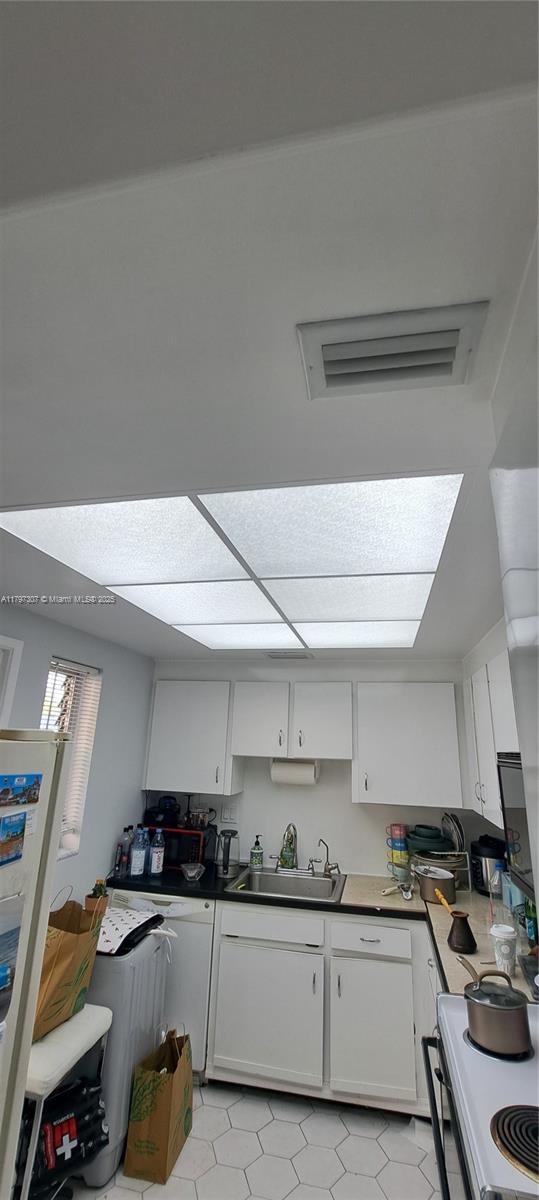 kitchen featuring a sink, dark countertops, white cabinets, white range with electric stovetop, and light tile patterned flooring
