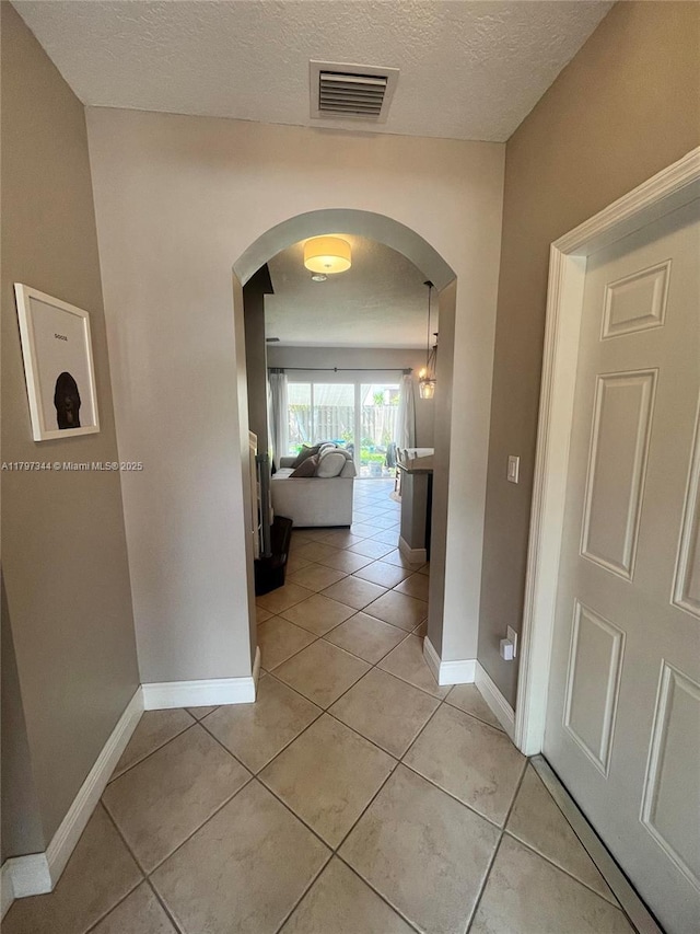 corridor with light tile patterned flooring, a textured ceiling, visible vents, arched walkways, and baseboards