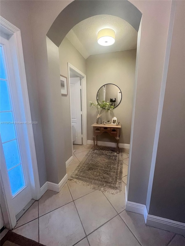 hall featuring arched walkways, tile patterned flooring, and baseboards