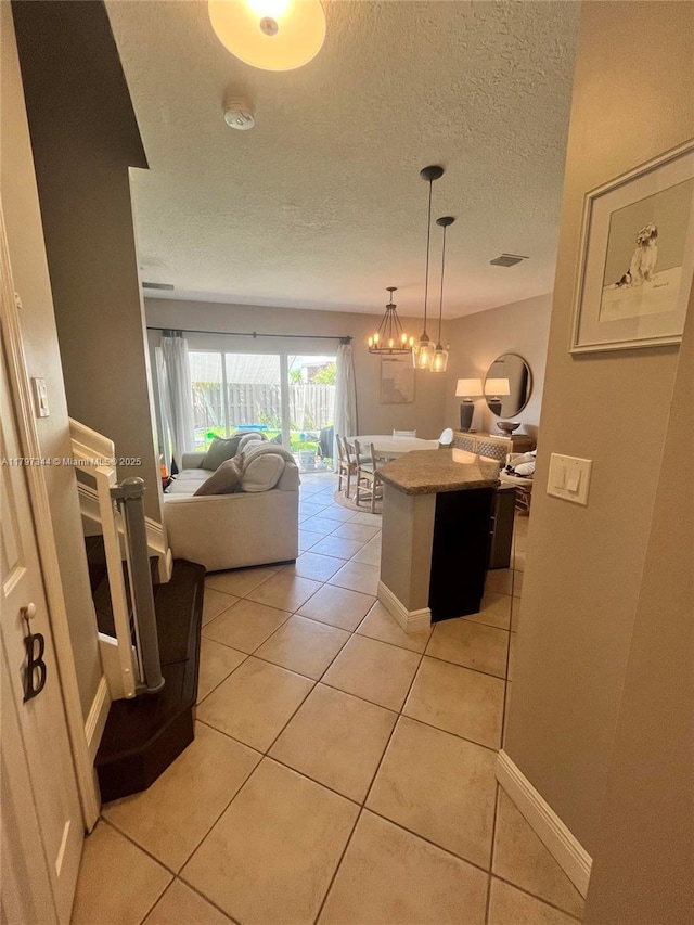 hallway with a textured ceiling, light tile patterned floors, baseboards, an inviting chandelier, and visible vents