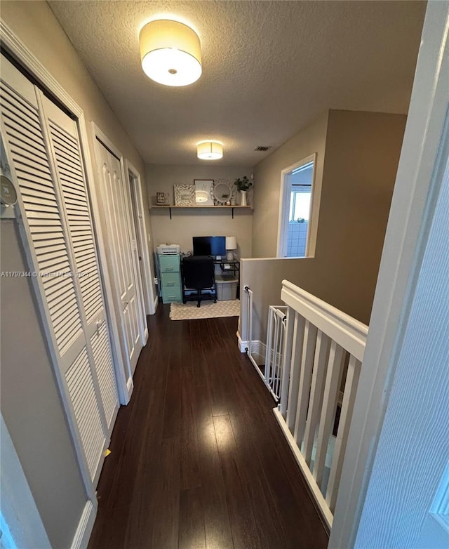 hallway featuring a textured ceiling, visible vents, baseboards, and wood-type flooring