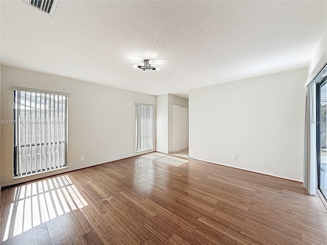 spare room featuring plenty of natural light, visible vents, wood finished floors, and a textured ceiling