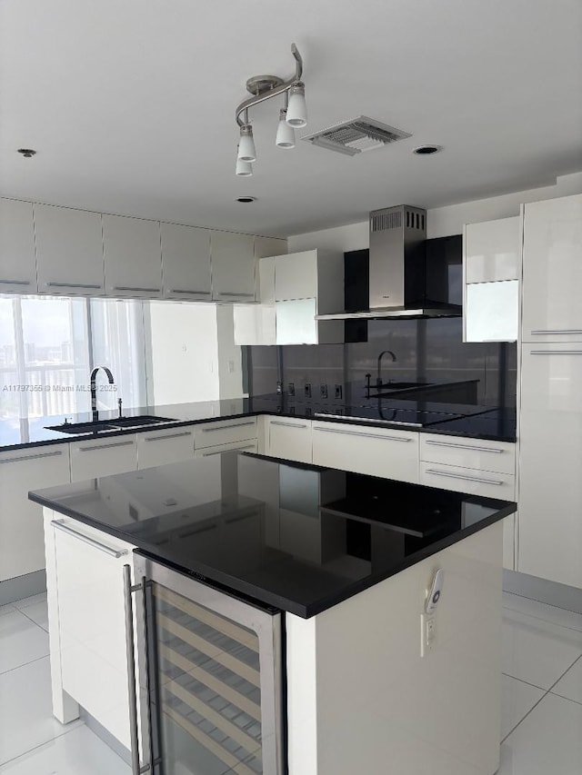 kitchen with wall chimney exhaust hood, dark countertops, beverage cooler, a center island, and white cabinetry