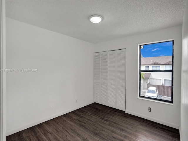 unfurnished bedroom featuring baseboards, dark wood-style flooring, a closet, and a textured ceiling