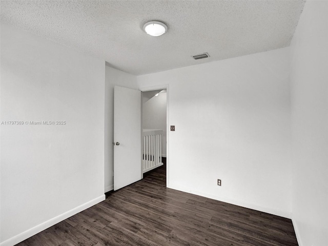 unfurnished room featuring a textured ceiling, visible vents, baseboards, and dark wood-type flooring