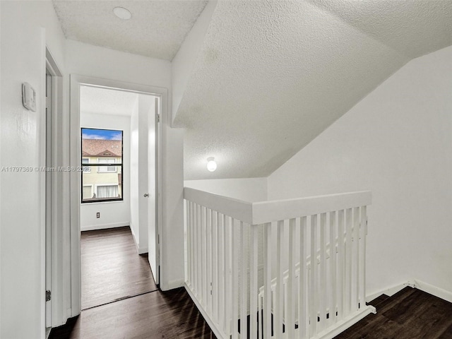 hall with a textured ceiling, lofted ceiling, wood finished floors, baseboards, and an upstairs landing
