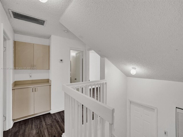 hall with a textured ceiling, an upstairs landing, visible vents, vaulted ceiling, and dark wood finished floors