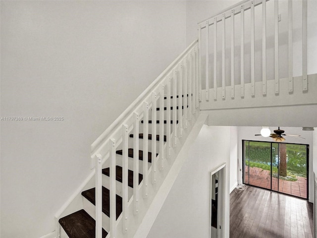 stairway featuring wood finished floors, a towering ceiling, a ceiling fan, and baseboards