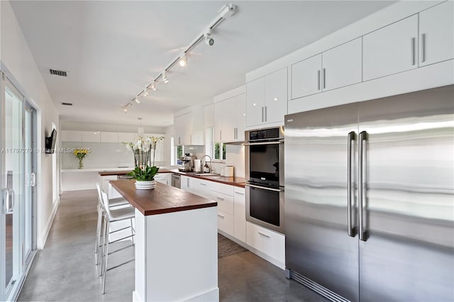 kitchen with wood counters, stainless steel appliances, finished concrete floors, and track lighting