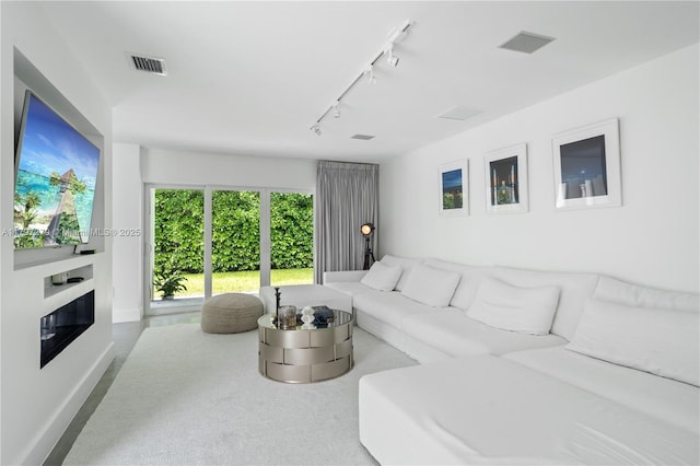 living area with rail lighting, baseboards, a glass covered fireplace, and visible vents