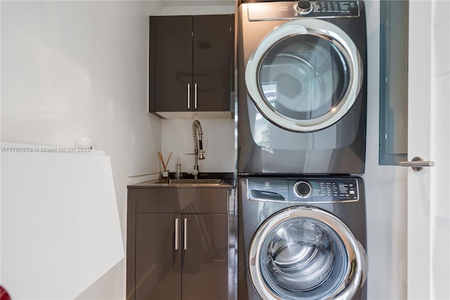 clothes washing area featuring a sink, stacked washer / drying machine, and cabinet space