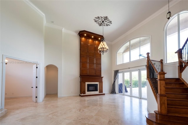 unfurnished living room with crown molding, a towering ceiling, arched walkways, and french doors