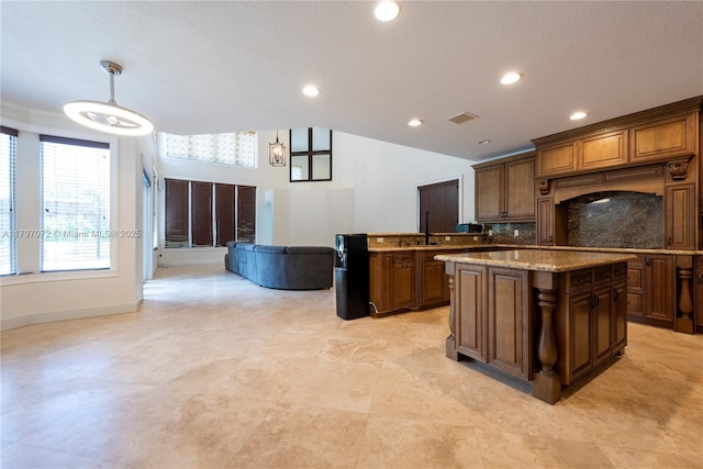 kitchen featuring a center island, open floor plan, pendant lighting, light stone countertops, and recessed lighting