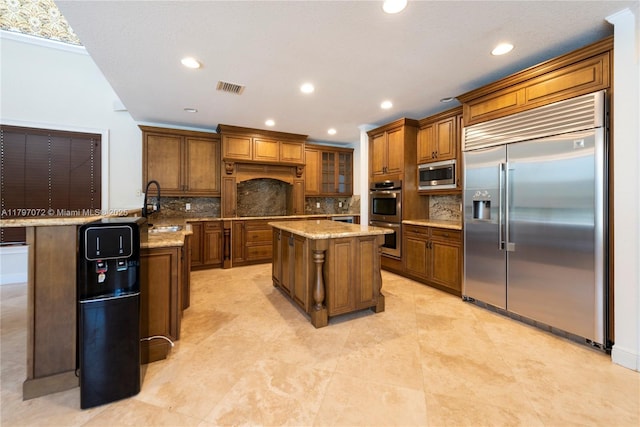 kitchen with brown cabinets, a sink, visible vents, built in appliances, and tasteful backsplash