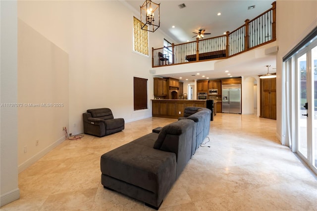living area featuring ceiling fan with notable chandelier, a towering ceiling, visible vents, arched walkways, and baseboards