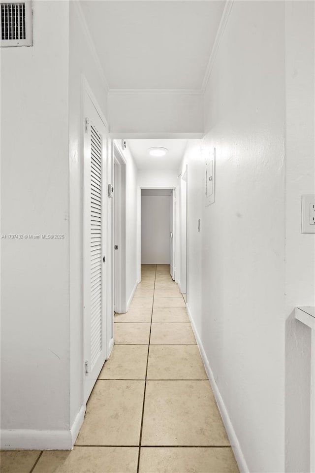 hallway with light tile patterned floors, ornamental molding, visible vents, and baseboards