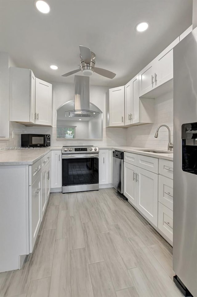 kitchen with a ceiling fan, stainless steel appliances, a sink, island range hood, and light countertops
